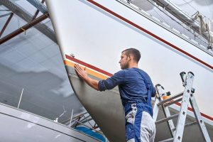 un ouvrier pose de l'adhésif sur la coque du bateau